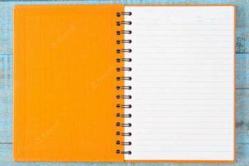 Caderno com capa laranja sob uma mesa cinza aberto.